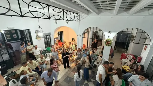 Grupo de personas de distintas edades compartiendo en un patio con sillas y guitarras en una convivencia festiva y animada en Badajoz