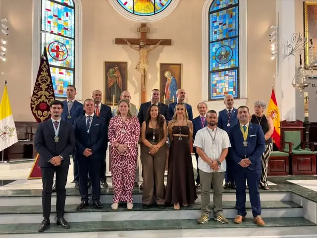 Grupo de personas vestidas formalmente posando en el altar mayor de una iglesia con vitrales y la bandera nacional al fondo
