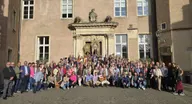 Gran grupo de personas de diversas edades posando frente a la entrada principal del castillo histórico con una carreta y banderas del Simpecado rociero