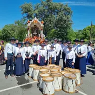Grupo de tamborileros vestidos con trajes tradicionales rocieros posan junto a una carreta decorada y varios tambores en el suelo bajo un cielo despejado