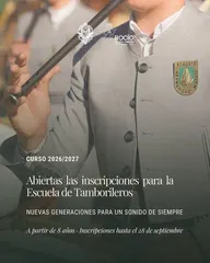 Persona vestida con traje gris claro y escudo de Hermandad Matriz de Almonte tocando un tamboril con baquetas negras
