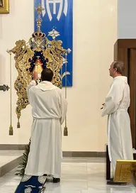 Dos sacerdotes vestidos de blanco bendicen el Simpecado ricamente decorado con detalles dorados y azul intenso en el altar de la hermandad