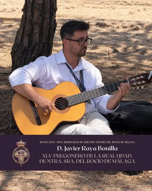 Hombre sentado bajo un pino tocando una guitarra clásica, vestido con camisa blanca y cordón tradicional de hermandad en un entorno natural seco