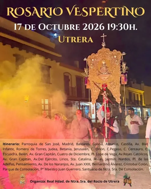 Personas portan un simpecado iluminado y envuelto en incienso durante un rosario vespertino en una calle de Utrera al anochecer