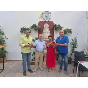 Cuatro personas posan en un patio con plantas y una imagen religiosa sosteniendo txistus donados a la Escuela de Tamborileros de la Hermandad
