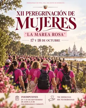 Grupo numeroso de mujeres vestidas con camisetas y pañuelos rosas caminando hacia la aldea del Rocío con la ermita visible al fondo bajo un cielo despejado