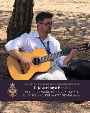 Hombre sentado bajo un pino tocando una guitarra clásica, vestido con camisa blanca y cordón tradicional de hermandad en un entorno natural seco