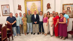 Doce personas posan sonrientes en un salón con cuadros religiosos y una imagen central de la Virgen del Rocío enmarcada en dorado