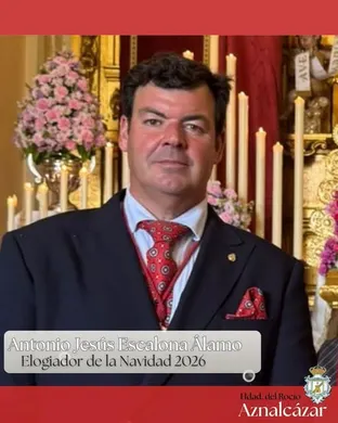 Hombre con traje oscuro y corbata roja posa en capilla decorada con flores y cirios frente a altar dorado en ambiente solemne