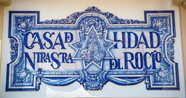 Fachada decorada con azulejos azules que muestran el nombre Casa Hermandad Nuestra Señora del Rocío con motivos ornamentales y religiosos en Morón de la Frontera
