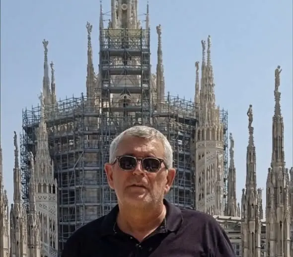 Hombre con gafas de sol y camiseta negra posando frente a una catedral gótica en restauración bajo un cielo despejado
