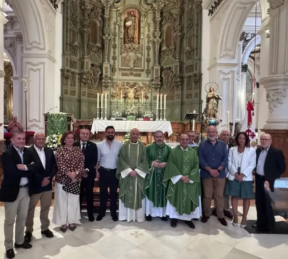 Grupo de personas, entre ellas tres sacerdotes con casullas verdes, posan en el interior de una iglesia frente al altar mayor decorado con velas y una imagen religiosa
