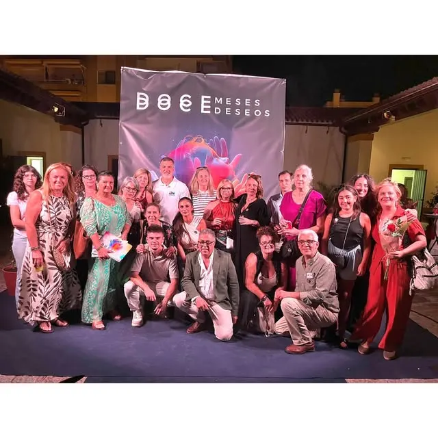 Grupo de personas posando sonrientes frente a un cartel que dice doce meses doce deseos en un evento benéfico en Jerez