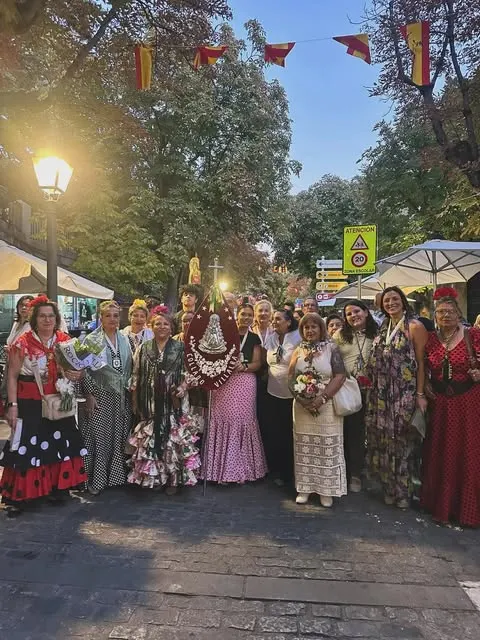 Grupo de personas vestidas con trajes tradicionales rocieros posan juntas en una calle decorada con banderas al atardecer durante una celebración religiosa