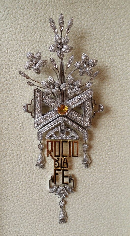 Broche que en agradecimiento y como recuerdo se le ha ofrecido en acción de gracias a la Stma. Virgen del Rocío.  ROCÍO DE LA FE, del cual nace un gran lazo que une a cinco jazmines que representan a las cinco Hermandades Filiales de la Diócesis de Córdoba.
